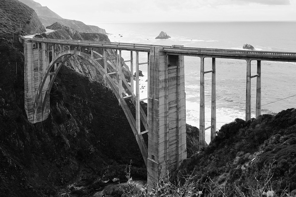 Black and white landscape photo of Bixby Creek Bridge. A reinforced concrete open-spandrel arch bridge in Monterey County, California.