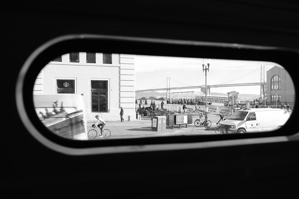 Black and white landscape photo of the San Francisco–Oakland Bay Bridge taken through the thin top rounded window of the historic street car.