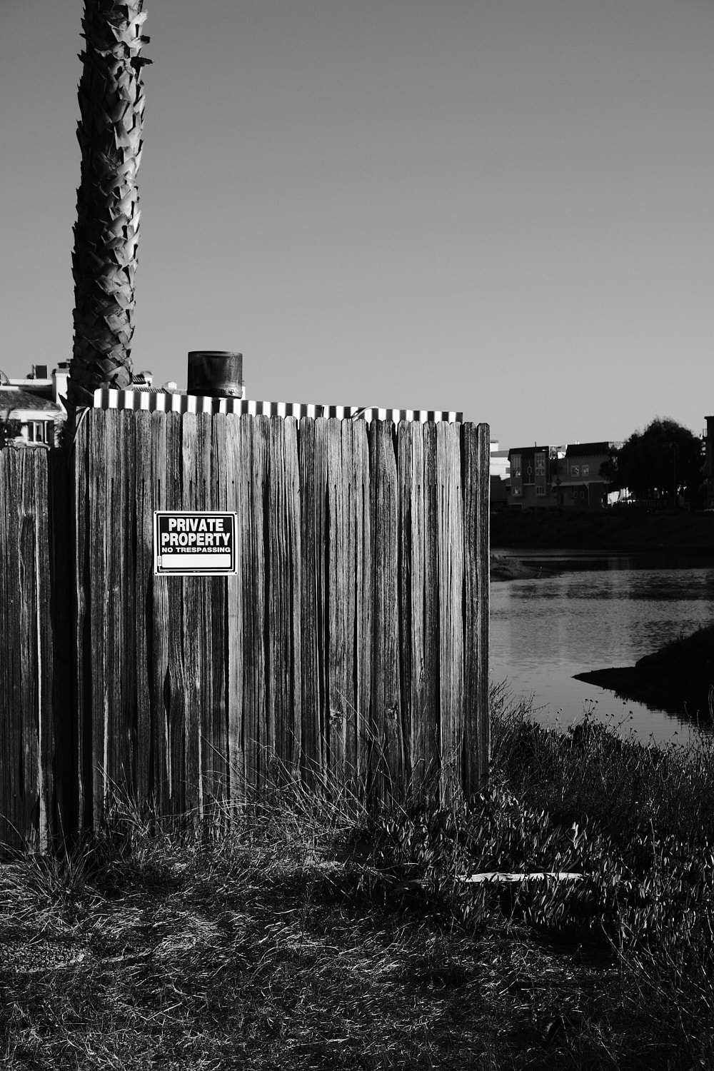 Black and white portrait photo of a fence with a PRIVATE PROPERTY No Tresspassing sign.